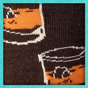 Close up image of a brown and orange sock featuring a whiskey glass design