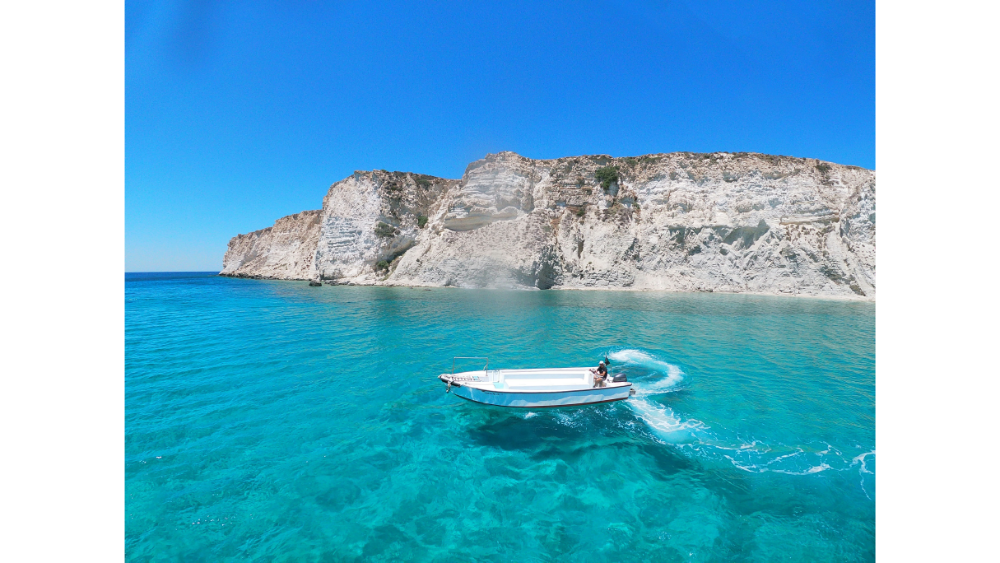 Speedboat cruising over the bright blue water near the white cliffs of Crete, with a couple on board enjoying the sunshine and open sea.