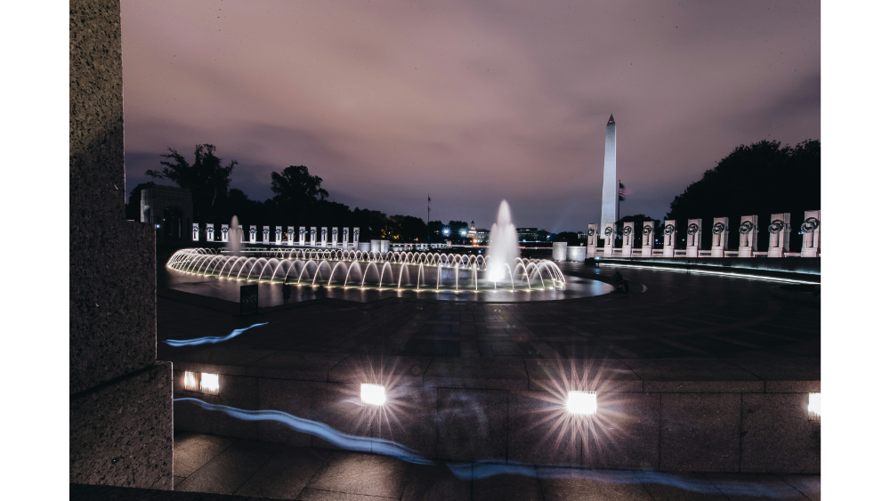 Night view of the World War II Memorial fountain in Washington, D.C., with the Washington Monument in the background.