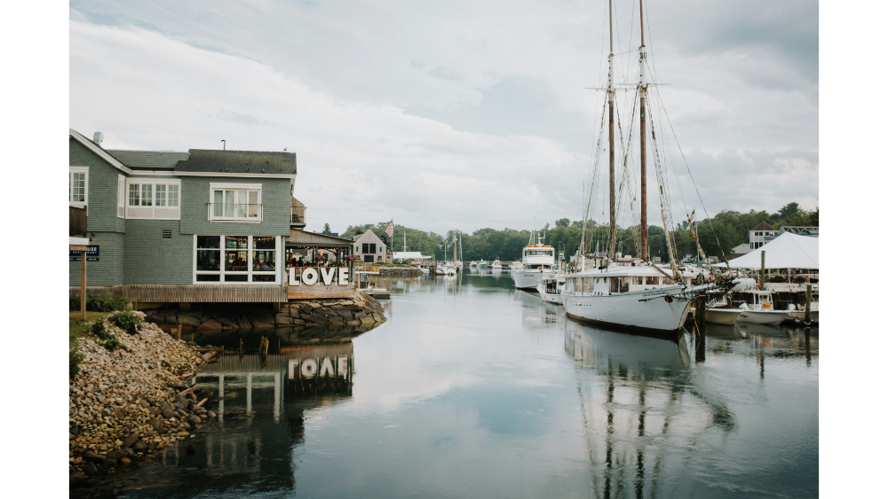 Dockside scene with boats and waterfront buildings in a small harbor town, with the word “LOVE” displayed on a patio.