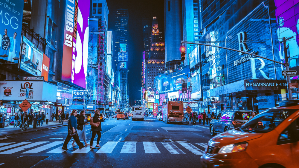 Night view of Times Square in New York City with bright neon lights, digital billboards, yellow taxis, and crowds of people crossing the street.