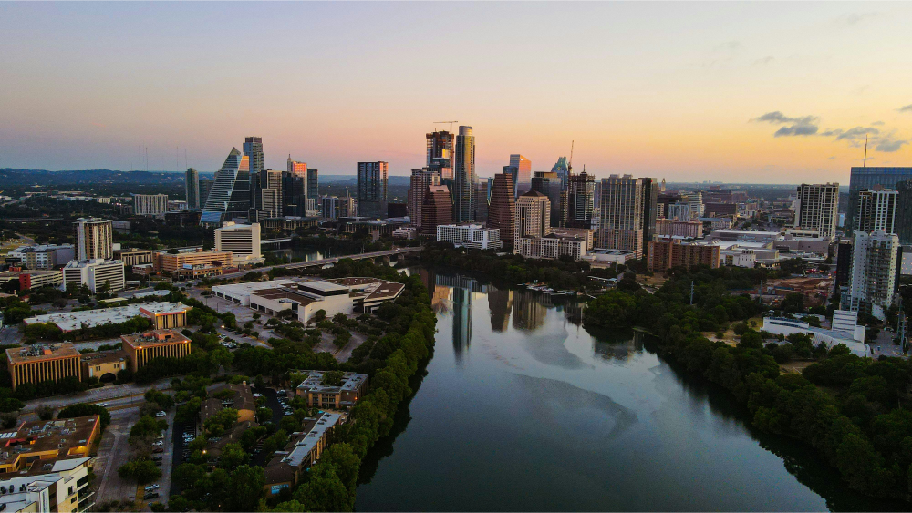 Aerial view of downtown Austin, Texas, with high-rise buildings and a river reflecting the warm colors of sunset.