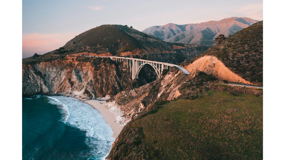 Dramatic coastline with a scenic arched bridge spanning rugged cliffs above crashing ocean waves.