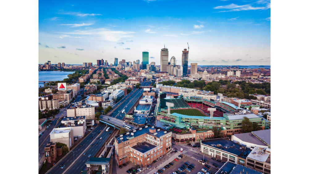 Aerial view of downtown Boston, Massachusetts, showing the skyline, highways, and the historic Fenway Park baseball stadium.