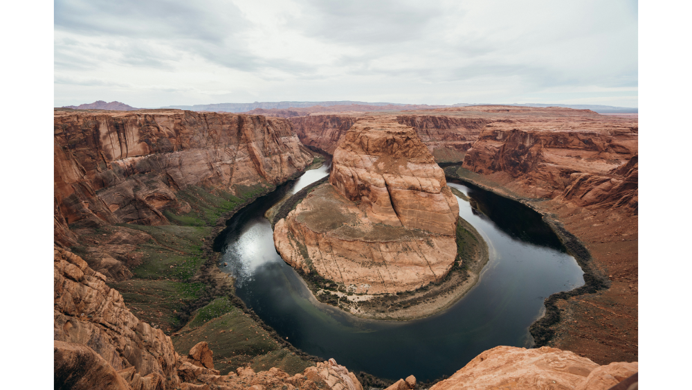 Scenic overlook of Horseshoe Bend where the Colorado River curves sharply through red canyon walls under a cloudy sky.