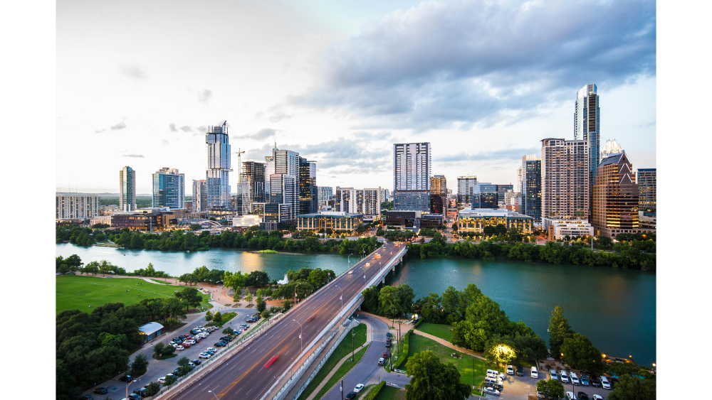Modern city skyline with tall buildings and a river running through the downtown area at dusk.