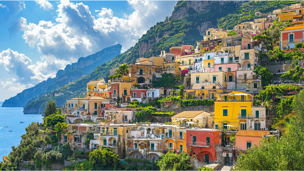 Vibrant, colorful buildings stacked on a steep coastal hillside overlooking a blue sea and lush green cliffs.