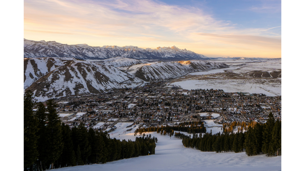 Panoramic view of Jackson Hole in winter, showing snow-covered mountains, a ski slope, and a town nestled in the valley.