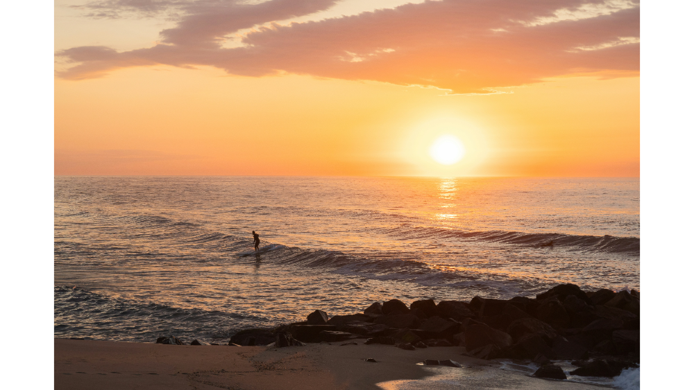 Serene beach scene at the Jersey Shore with a person standing in the water at sunset, golden light reflecting on the waves.