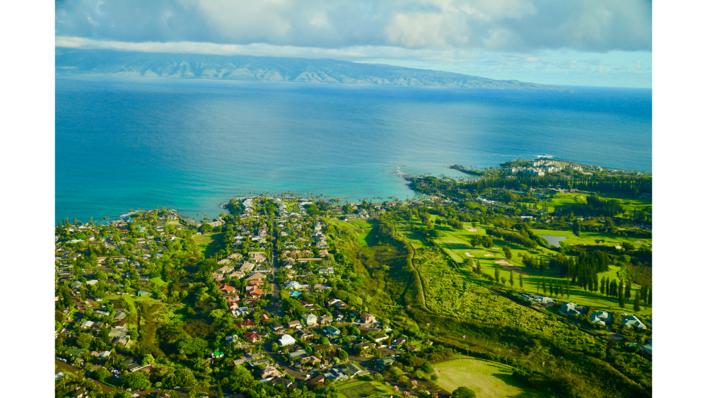 Aerial view of coastal town and lush landscape in Maui, Hawaii with the ocean in the background.