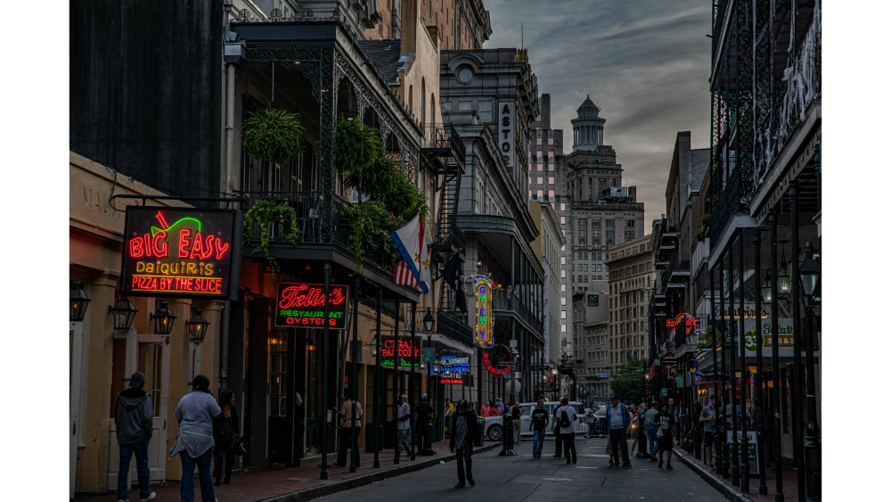 Lively street scene in New Orleans with neon signs, historic buildings, and people walking.