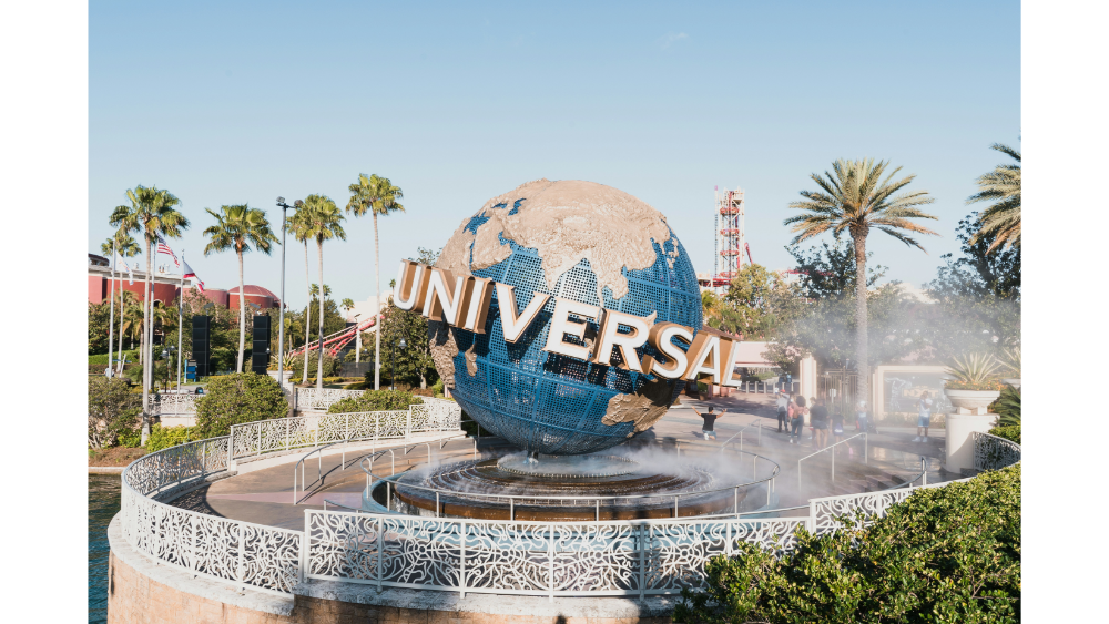 Large rotating globe sculpture with "Universal" lettering at the entrance of Universal Studios theme park surrounded by palm trees and mist.