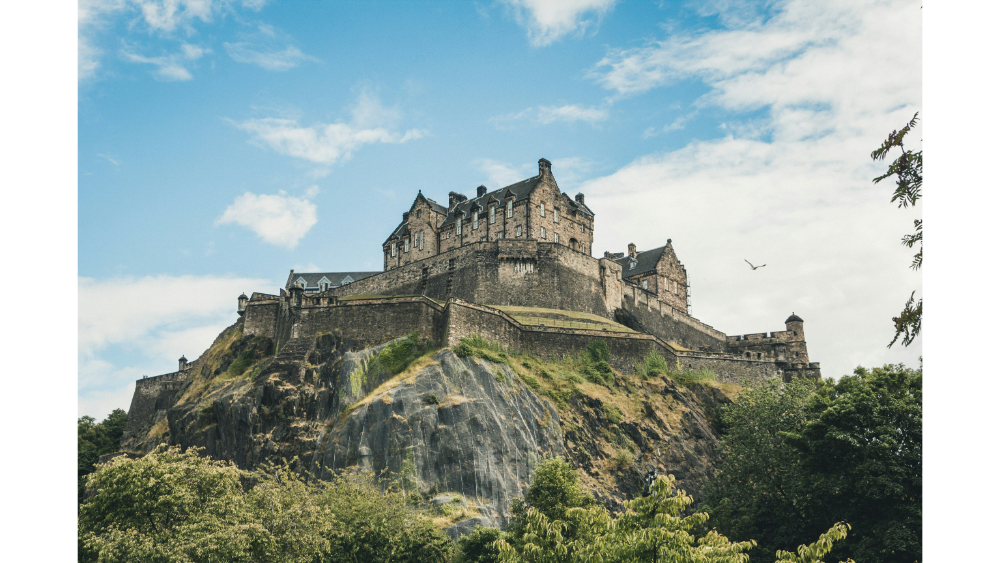 Ancient stone castle perched on a rocky hilltop with a backdrop of blue sky and scattered clouds.