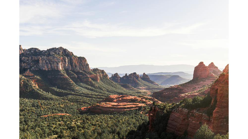 A wide view of Sedona’s red rock formations and green forested landscape during daylight.