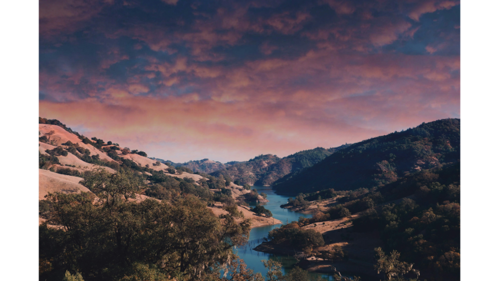 A scenic view of rolling hills and a winding river under a vibrant sunset sky in Sonoma, California.