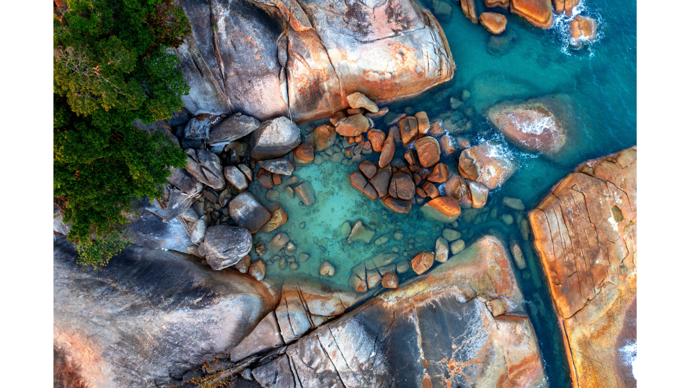 Aerial view of turquoise water surrounded by large coastal boulders and rocky terrain.