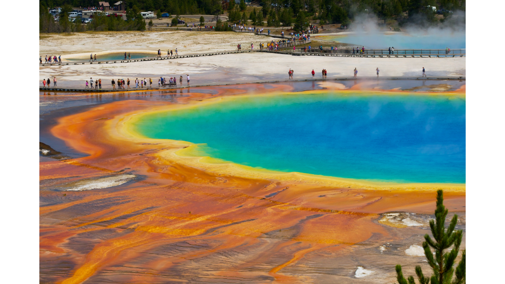 Brightly colored geothermal hot spring with vivid orange, yellow, green, and blue hues, surrounded by walkways and tourists.