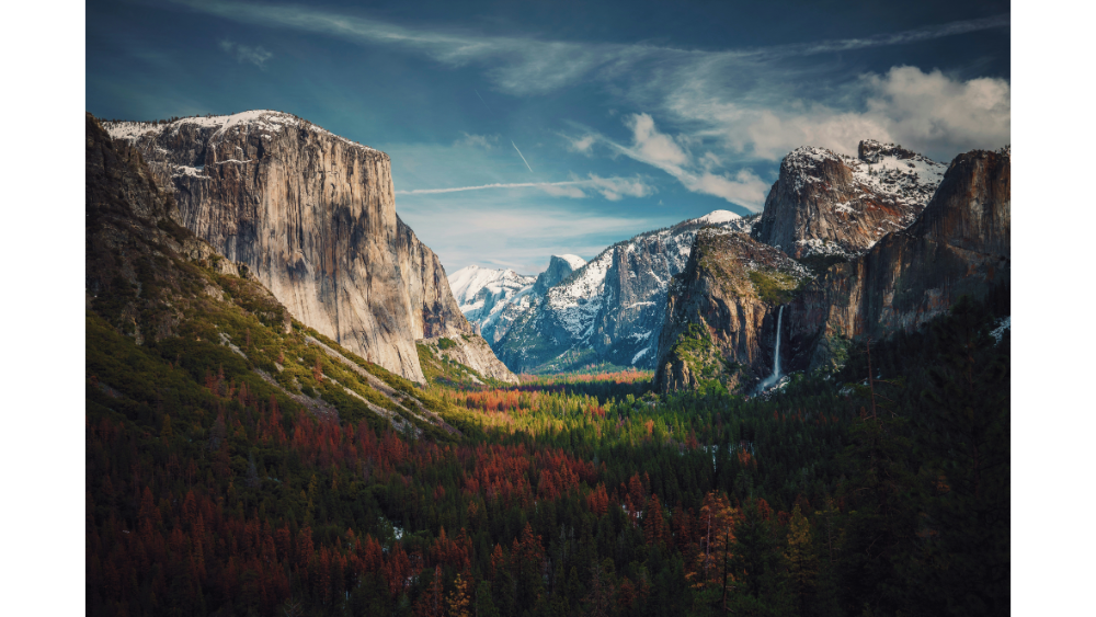 Stunning view of Yosemite National Park featuring El Capitan, Half Dome, snow-covered peaks, and a forested valley.