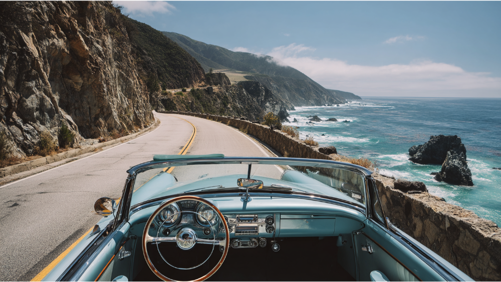 View from a classic convertible driving along the scenic Pacific Coast Highway beside rocky cliffs and ocean waves.