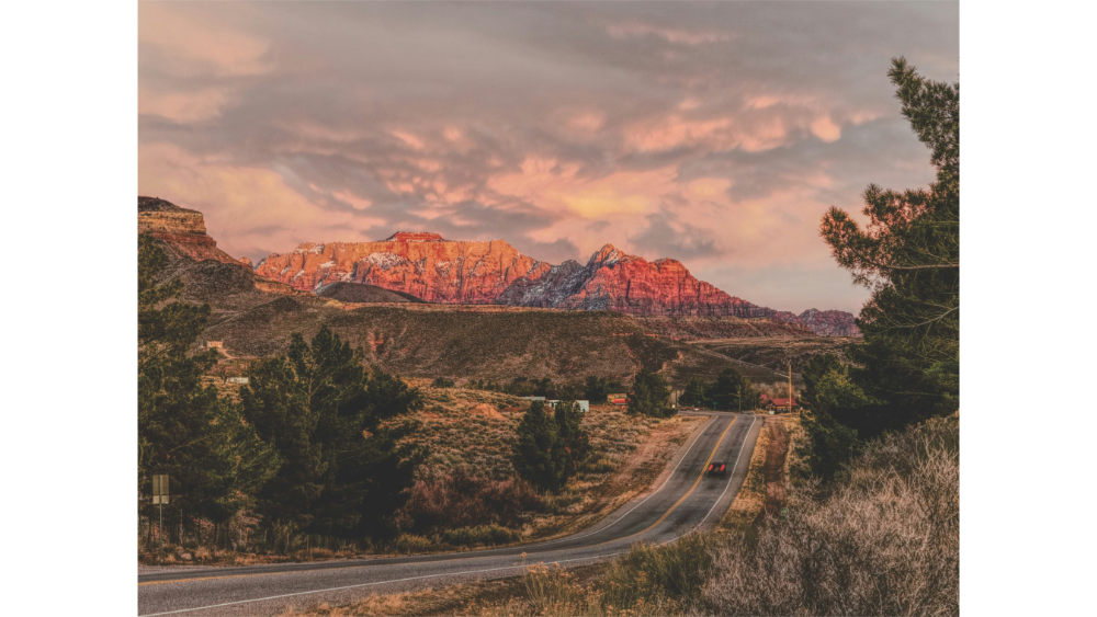 Winding road leading toward dramatic red rock formations in Zion National Park under a glowing sunset sky.