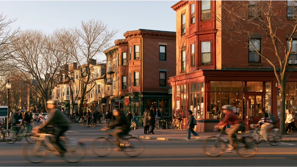 Cambridge Massachusetts neighborhood streets with residential buildings, commercial squares, pedestrians, and transit activity
