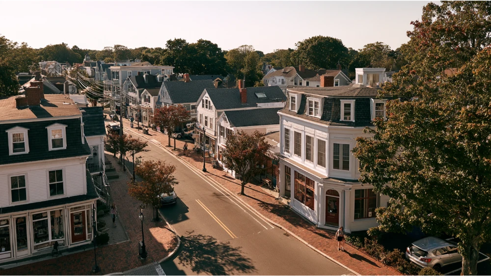 A traditional New England village street in Warwick, Rhode Island, featuring historic homes, local shops, sidewalks, and established neighborhood architecture.