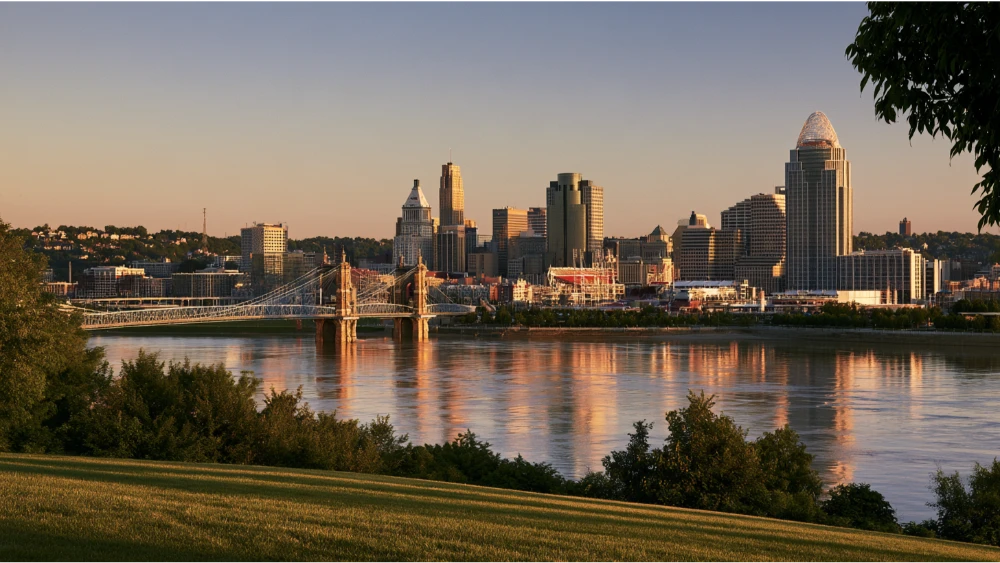 Cincinnati, Ohio skyline along the Ohio River with downtown buildings, riverfront parks, and the Roebling Suspension Bridge.