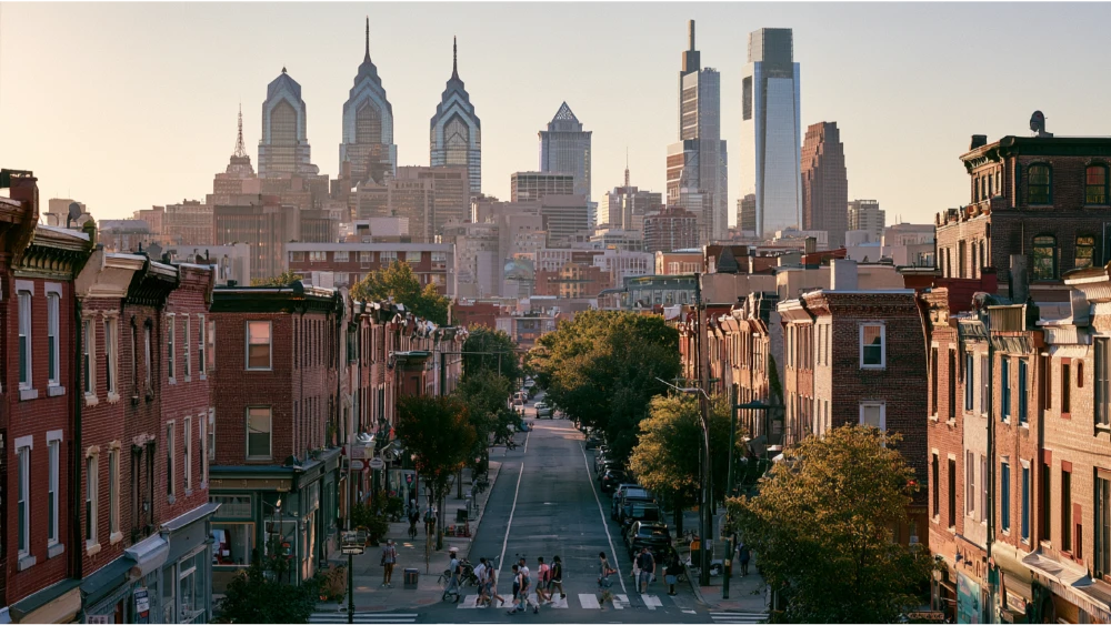 Philadelphia's Center City skyline rising above historic brick buildings, tree-lined streets, and lively neighborhood blocks.